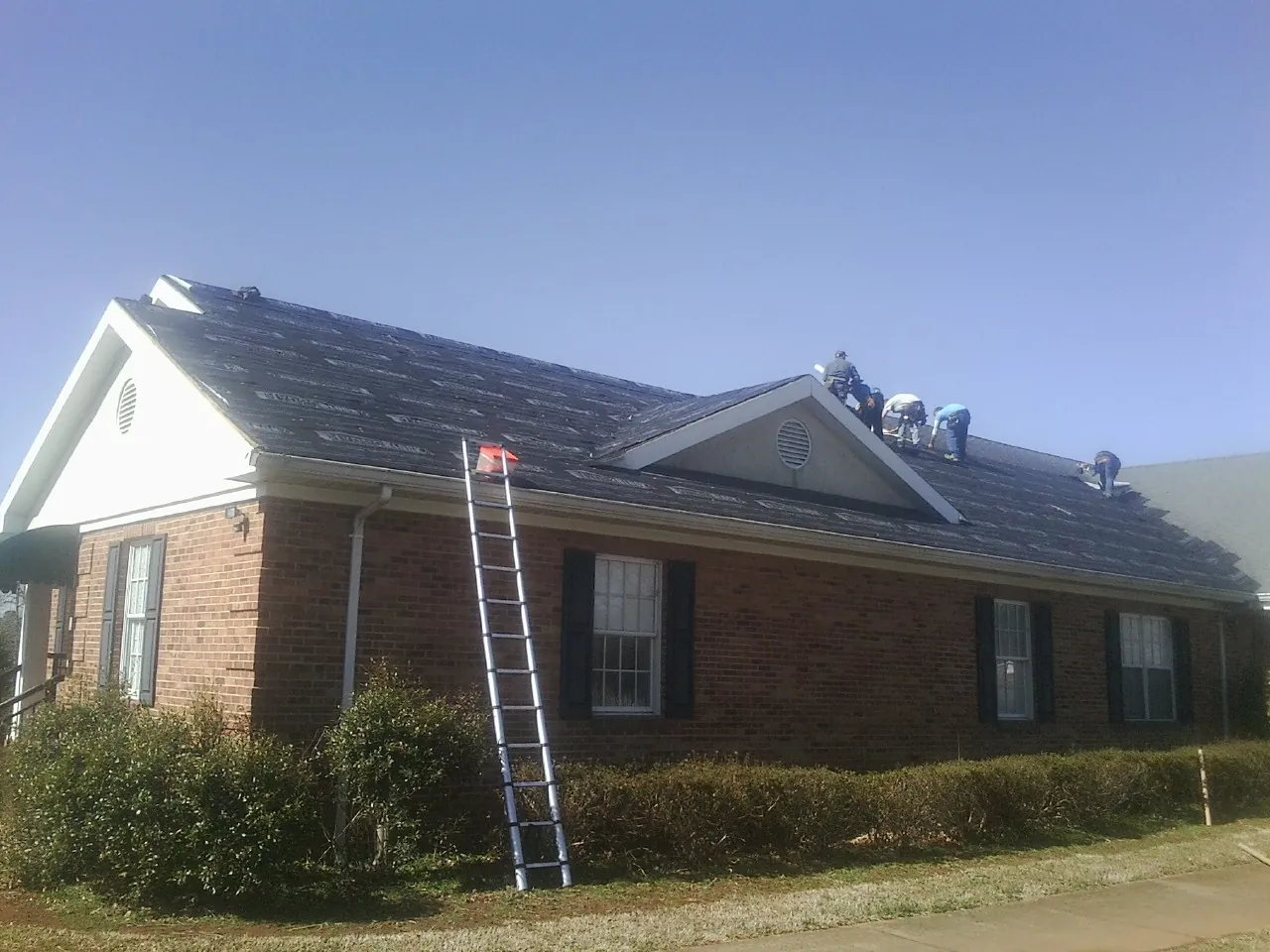 Crew tearing shingles off a brick ranch roof with a ladder set — Emergency Roof Repair work by our crew in Rock Stream