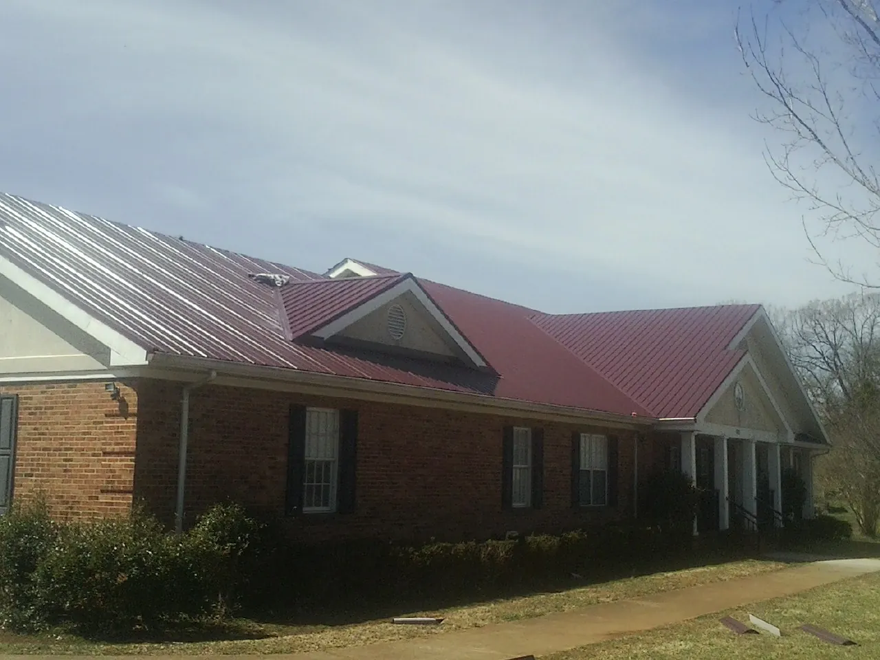 Red metal roof with gabled entries on a long brick building, from a Hail Damage Roof Repair job in Rock Stream