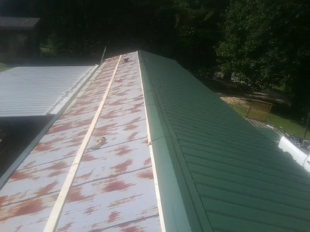 Old rusted panels beside newly installed green metal roofing in Rock Stream