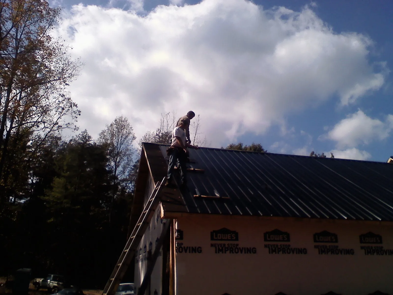Roofer fastening dark metal panels high against a cloudy sky, from a Roof Inspection job in Rock Stream