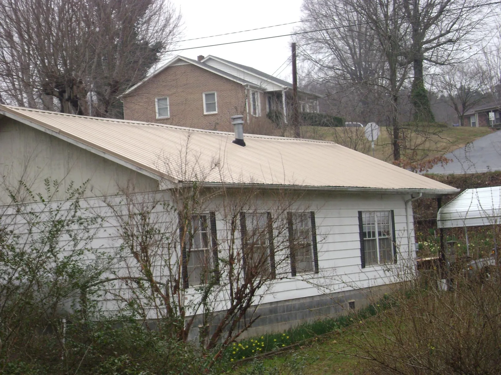 Tan metal roof on a white sided house set into a hillside — Commercial Roofing by Roofing Brothers in Rock Stream