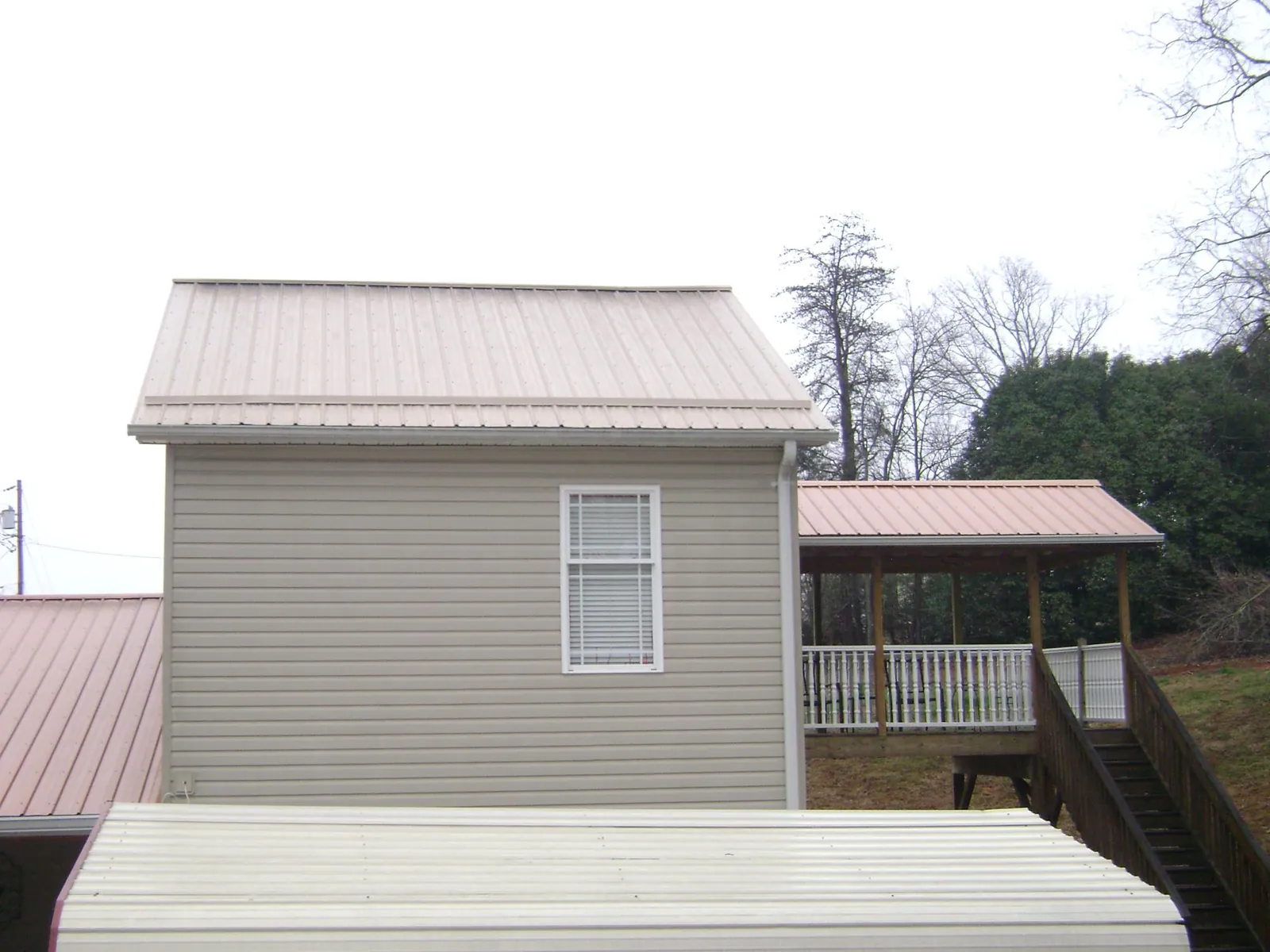 Tan metal roofs on a two story addition and attached porch, from a Roof Replacement job in Rock Stream